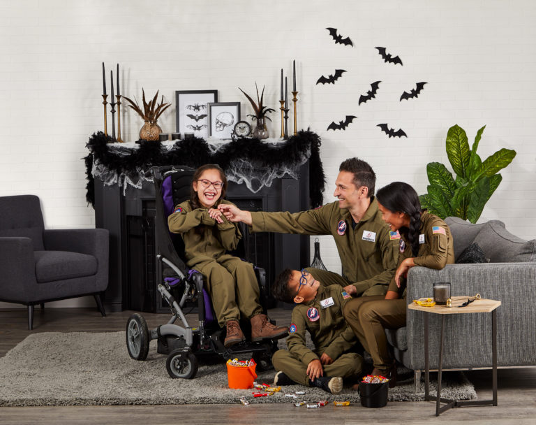 Two kids and their parents dressed up in Ghostbuster costumes. The child on the left side is using a wheelchair.