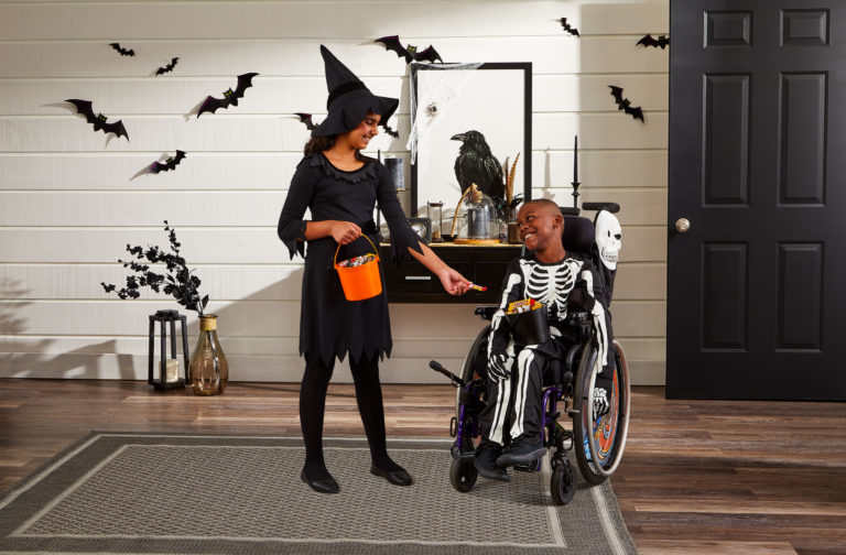 A kid sits on a wheel chair and having fun with treat or trick.
